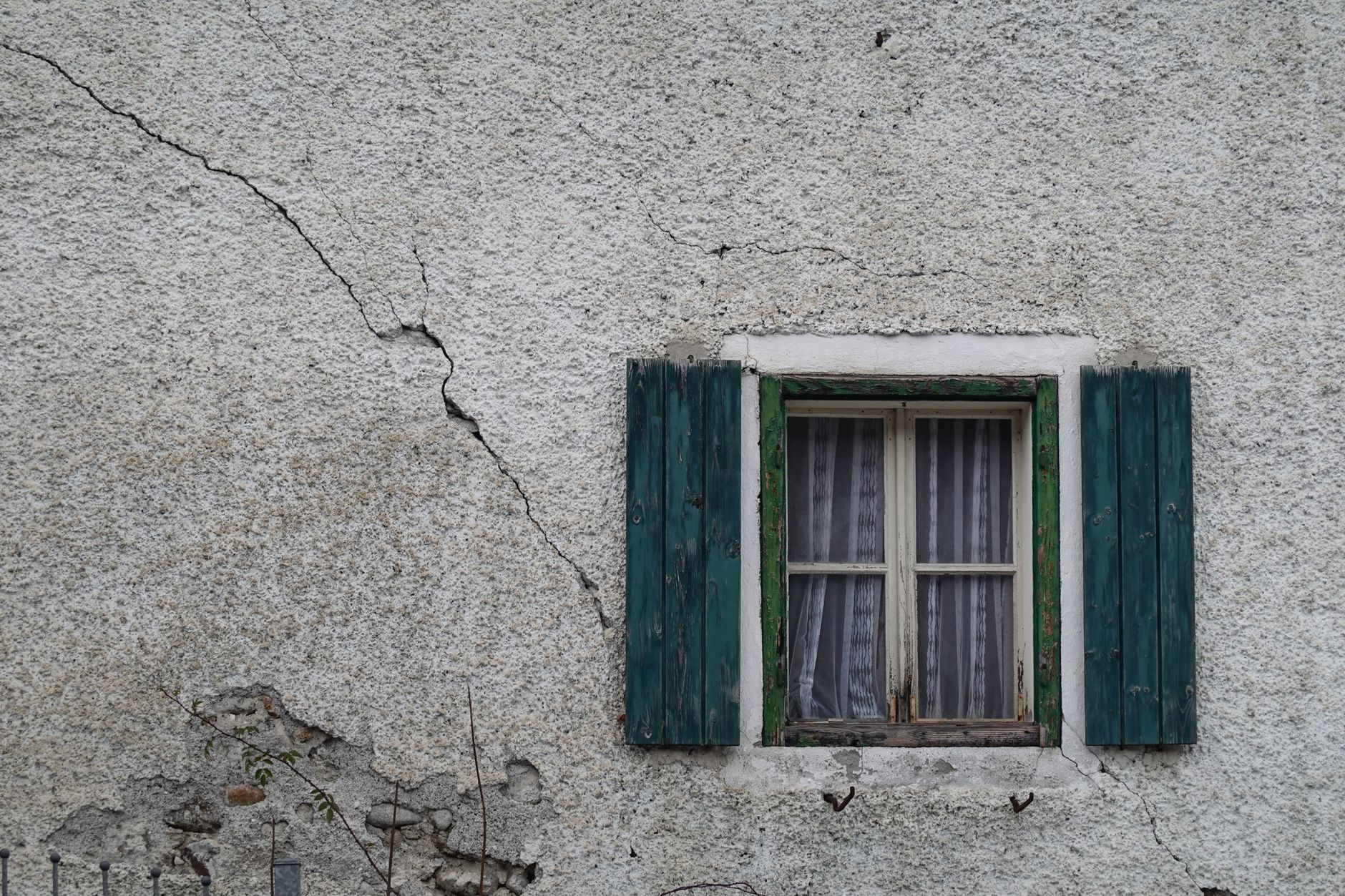 Old cracked concrete wall with a rustic window and green shutters