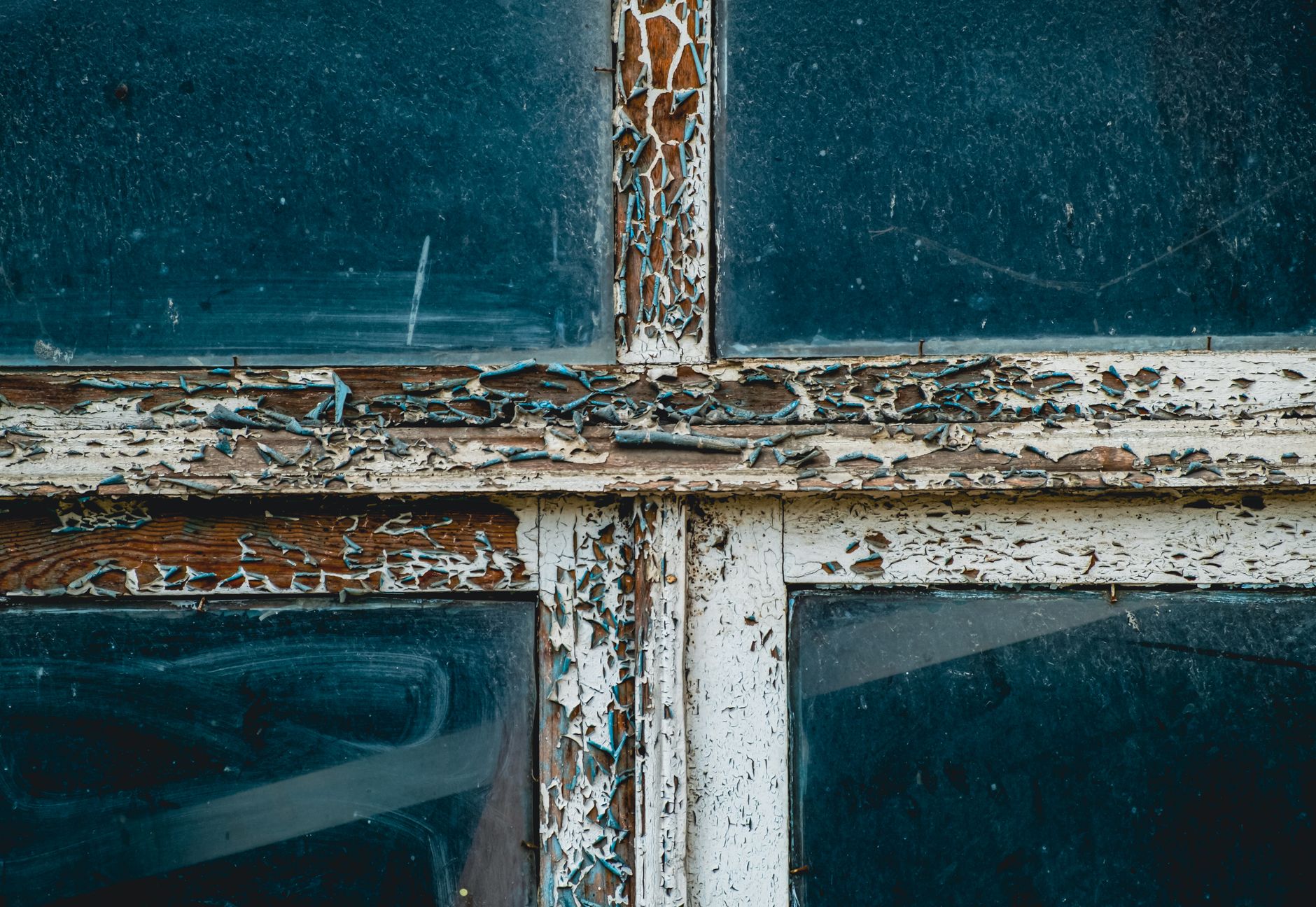 Detailed view of peeling paint on a rustic wooden window frame, showcasing texture and decay