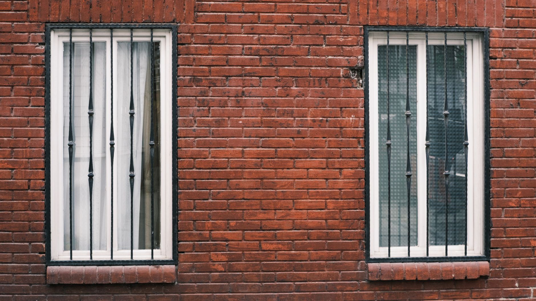 Red brick wall with two barred windows in urban setting